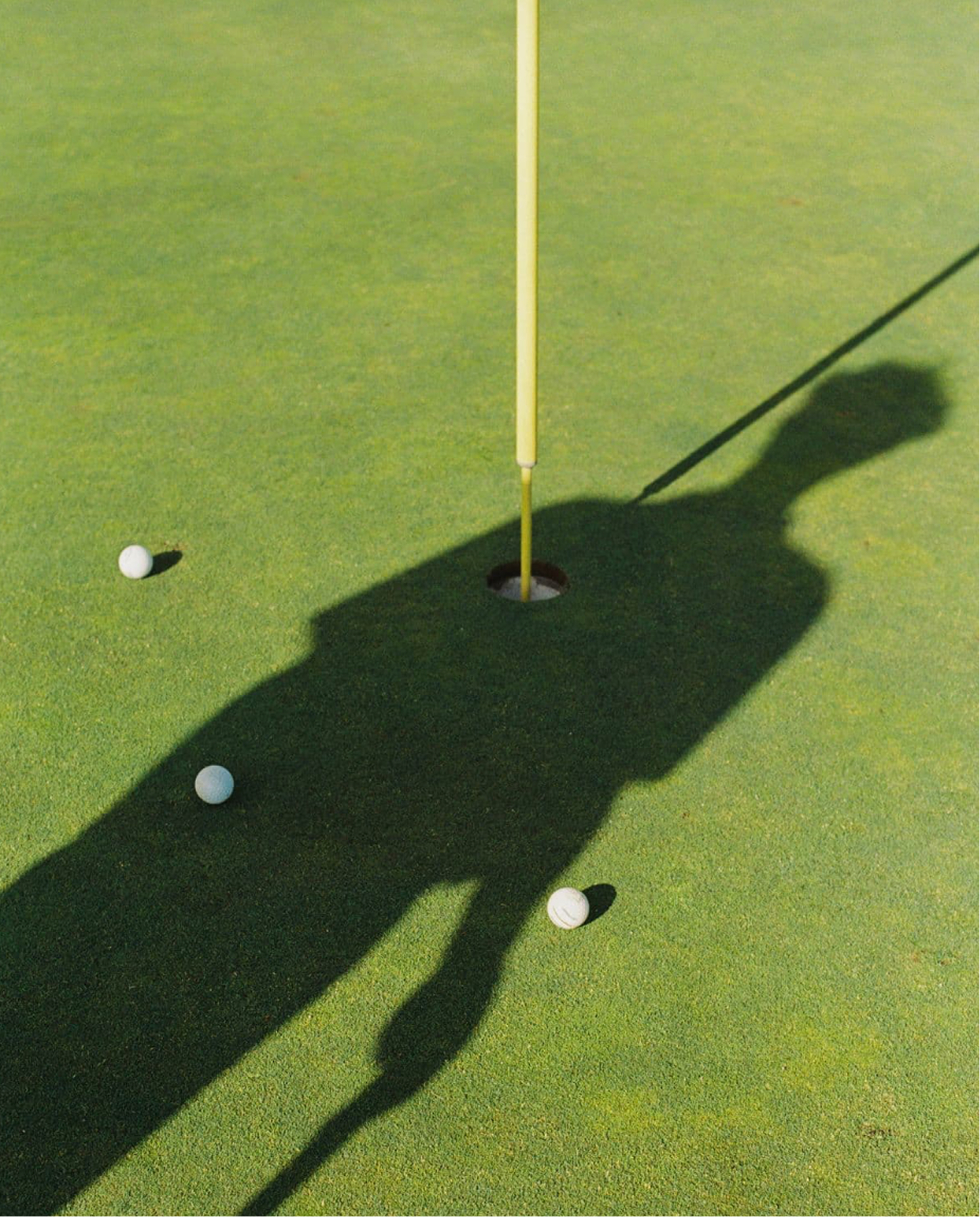 Shadow of a golfer standing near a putting hole with golf balls on the green