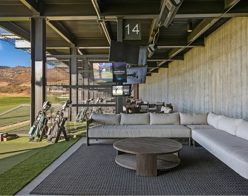 Covered golf hitting bay with lounge seating and television screens at ParOne