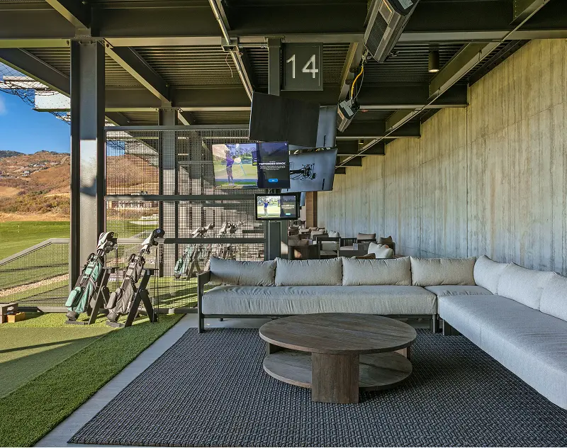 Covered golf hitting bay with lounge seating and television screens at ParOne