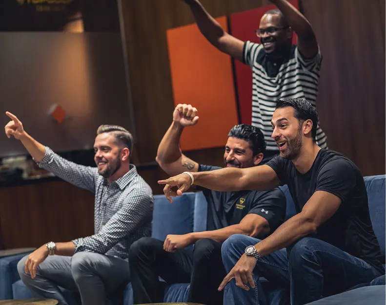 Group of friends cheering and watching a game inside a clubhouse lounge