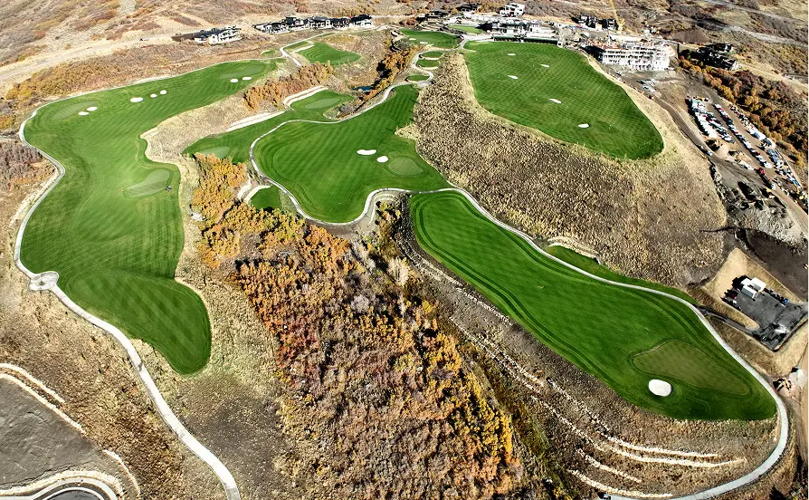 Aerial view of a short golf course with greens, fairways, and surrounding mountain terrain