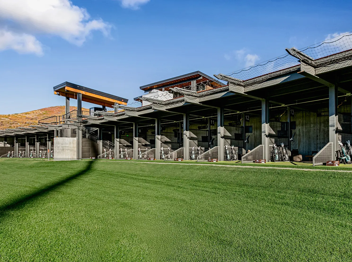 Outdoor golf hitting bays and clubhouse exterior with turf practice area