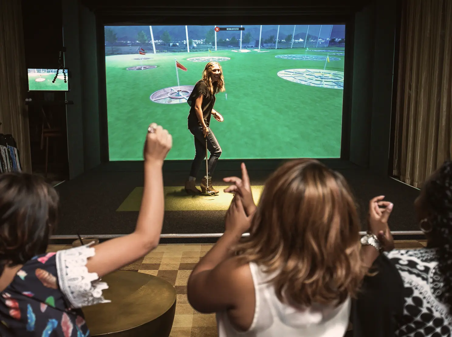 People watching and cheering during an indoor golf simulator experience