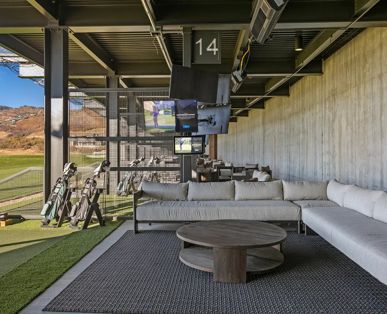 Covered golf hitting bay with lounge seating and television screens at ParOne
