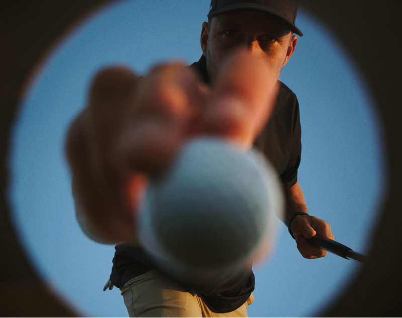 Golfer placing a golf ball on a tee viewed from inside the cup